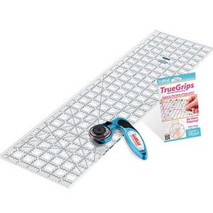 Op de afbeelding: Een quiltset met een doorzichtige acryl liniaal met rasterlijnen, een blauwe roterende snijder en een True Grips-verpakking. De roterende snijder heeft een zwart mes en een blauwe handgreep. De True Grips-verpakking heeft tekst en een handillustratie.