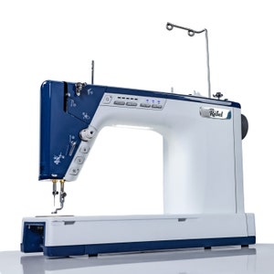 May include: A blue and white sewing machine with a needle and thread in place. The machine has a digital display and a variety of buttons and controls. The brand name "Rebel" is visible on the front of the machine.