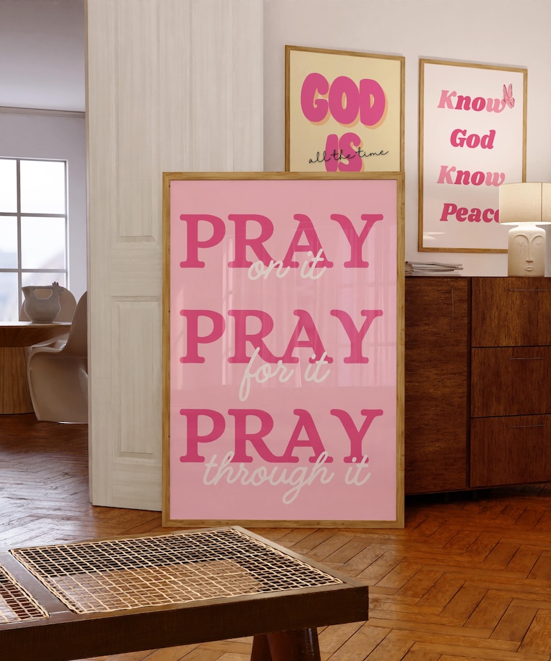 Może przedstawiać: Oprawiony r&oacute;żowy plakat z napisem "PRAY on it, PRAY for it, PRAY through it" w r&oacute;żowych literach. W tle widoczne są dwa inne oprawione plakaty z inspirującym tekstem. Pok&oacute;j ma drewniane podłogi.