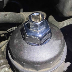 May include: A chrome oil filter wrench with a hexagonal shape, designed to fit over an oil filter cap. The wrench is placed on top of a black oil filter cap.