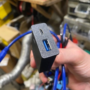 May include: A black USB hub with a USB-C port and a USB-A port. The hub is connected to a blue cable.