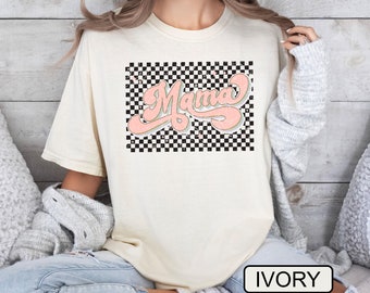 May include: A white t-shirt with a pink "Mama" graphic on a black and white checkered background. The shirt is labeled "IVORY".
