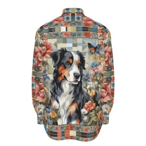Puede incluir: Una camisa de manga larga con botones y un estampado floral colorido con un perro negro, marrón y blanco en el centro. El perro está rodeado de flores y una mariposa.
