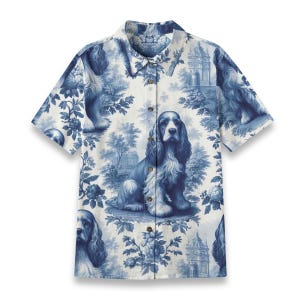Puede incluir: Camisa de manga corta con estampado azul y blanco de toile de Jouy. El diseño presenta Cocker Spaniels, elementos florales y escenas arquitectónicas. Cuello clásico y cierre de botones.