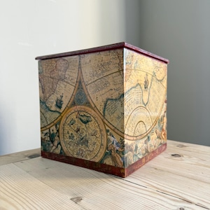 May include: A square wooden box featuring a vintage-style map print with beige, brown, and gold tones. The surface displays intricate illustrations of sea creatures, celestial patterns, and the text Magalla Terra. It has a dark red trim.