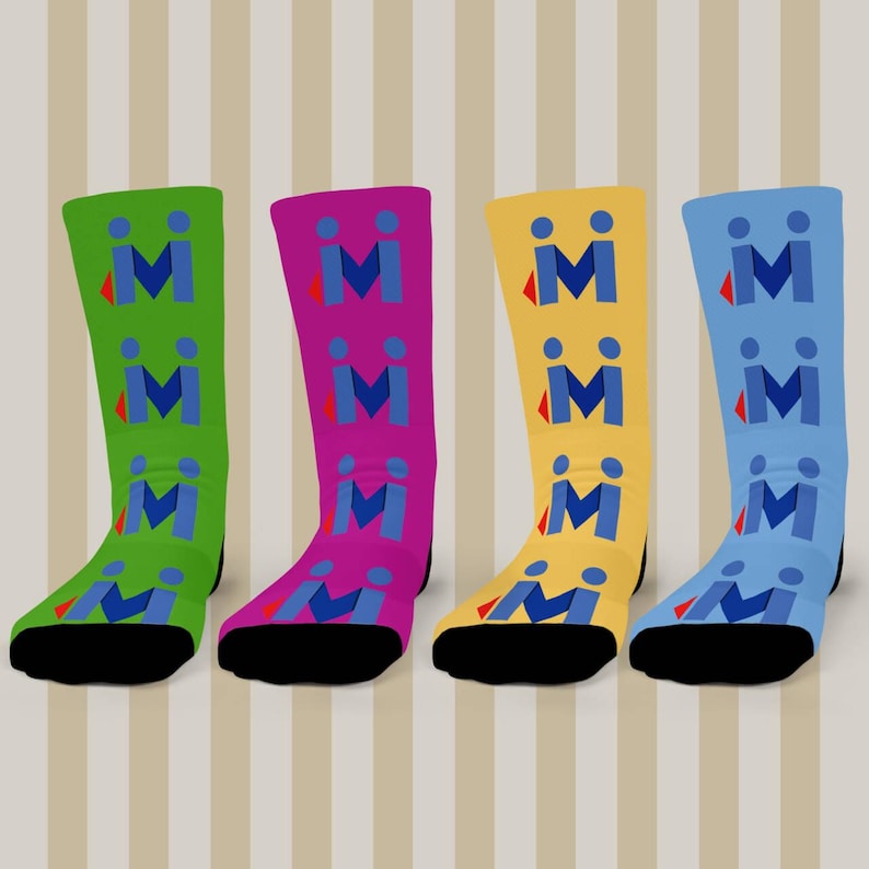 May include: Four brightly coloured socks, each in a different shade: green, purple, yellow, and blue. Each sock displays a repeating pattern of blue "M" shapes with a red accent. The socks have black toes and heels.