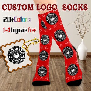 May include: Red custom logo socks with black heels and toes. The socks feature a repeating circular logo with a coffee cup design and the text "COMPANY YOUR SLOGAN". The text "CUSTOM LOGO SOCKS", "20+ Colors", and "1-4 Logo are Free" are also visible.