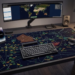 Puede incluir: Una moderna configuración de escritorio con un monitor curvo que muestra un mapa del mundo, un teclado negro y un ratón. Una gran alfombrilla de escritorio con cartas de aviación, un smartphone, altavoces y una lámpara de escritorio completan el espacio de trabajo. El escritorio es de madera.