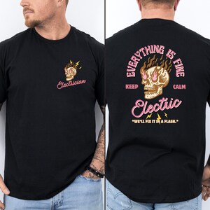 Könnte beinhalten: Schwarzes T-Shirt mit einem Totenkopf-Motiv und dem Text "Electrician" auf der Vorderseite. Die Rückseite des Shirts zeigt ein Totenkopf-Motiv mit Flammen und dem Text "Everything is fine keep calm Electric" und "We'll fix it in a flash."