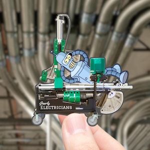 May include: A novelty pin featuring a cartoon robot character resting on a small cart. The cart is black with green accents and the words "Gnarly Electricians" printed on the side. The background shows a network of gray pipes.