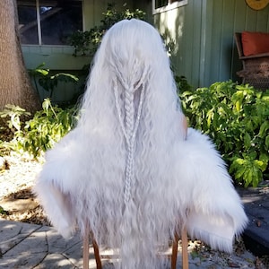 May include: A long, white wig with a braided design. The wig is styled in loose waves and has a natural, flowing look.