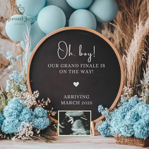 May include: A black chalkboard sign with white text announcing a baby's arrival. The sign reads "Oh. boy! Our grand finale is on the way! Arriving March 2025". The sign is surrounded by blue and white flowers and blue balloons.