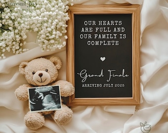 May include: A framed chalkboard sign with the text "Our hearts are full and our family is complete. Grand Finale Arriving July 2025." A teddy bear holding an ultrasound image is in the foreground.