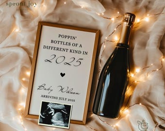 Puede incluir: Un cartel enmarcado en blanco con texto negro que dice "Poppin' Bottles of a Different Kind in 2025" con un corazón negro y el texto "Baby Wilson Arriving July 2025". Una imagen de ultrasonido en blanco y negro está debajo del texto. Una botella de champán está en el fondo.