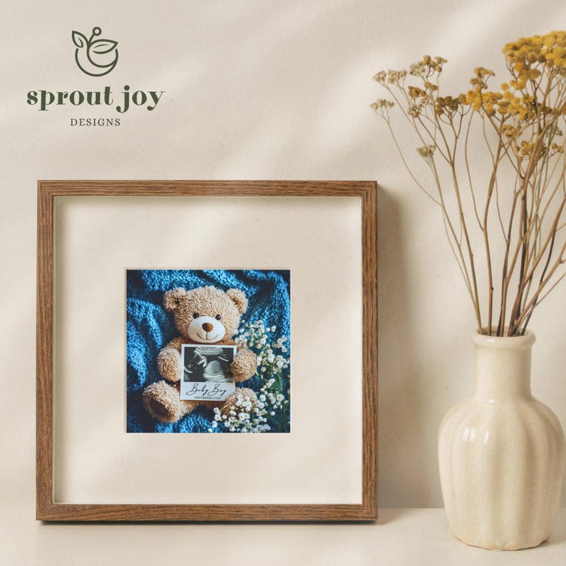 May include: A framed photo of a teddy bear holding a sonogram image with the text "Baby Boy" on a blue blanket. The frame is brown wood with a white mat.