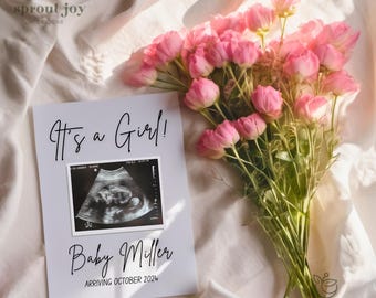 Puede incluir: Una tarjeta blanca con el texto "It's a Girl!" y "Baby Miller Arriving October 2024" con una imagen de ultrasonido en blanco y negro. La tarjeta está sobre un fondo de tela blanca con un ramo de flores rosas.