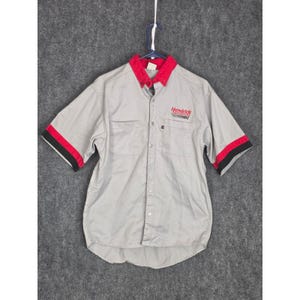 Peut inclure: Chemise grise à manches courtes avec col et détails des manches rouges. Le mot "Hendrick" est brodé en rouge sur la poitrine. Les manches ont une bande rouge avec un bord noir.