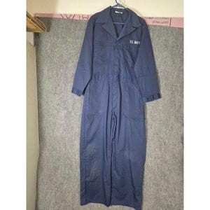 Può includere: Tuta blu navy con maniche lunghe, colletto e più tasche. Il testo "U.S. NAVY" è ricamato sul petto. L'indumento è appeso a un'appendiabiti.