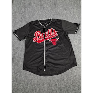 Op de afbeelding: Zwart honkbalshirt met witte bies en knoopsluiting. Het shirt heeft het woord "Bulls" in rood script over de borst, samen met een rood en wit stierenlogo. Korte mouwen.