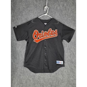 May include: Black baseball jersey with the word "Orioles" in orange script across the chest. The jersey has a button-down front and short sleeves. A small patch is visible on the lower left side.
