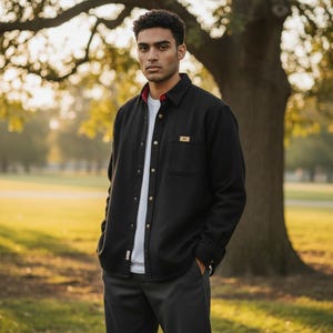 May include: A black long-sleeve button-down shirt with a pointed collar, a single chest pocket featuring a small rectangular tan label, and a white undershirt. The shirt has a red inner collar lining and light-colored buttons down the front placket.