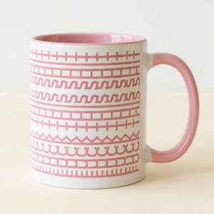 Könnte beinhalten: Eine weiße Keramik-Tasse mit schwarzem Henkel und dem Text "But First, Coffee" in schwarzer, fetter Schrift. Die Tasse steht auf einer weißen Oberfläche.
