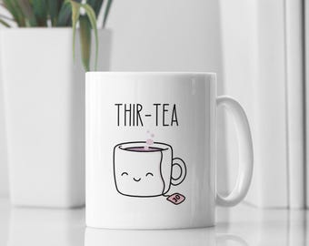 Könnte beinhalten: Weiße Keramiktasse mit schwarzem Umriss einer Teetasse und dem Text "THIR-TEA" mit einem rosa Teebeutel mit der Nummer 30 darauf.
