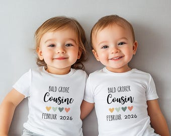 May include: Two young children wearing white t-shirts with the text "Bald Grobe Cousine" and "Bald Grober Cousin" in black script. Below the text are four colored hearts and the date "Februar 2026".