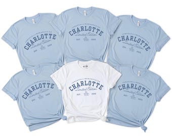 May include: Six light blue t-shirts with the text "CHARLOTTE Limited Edition EST. 2025" printed in navy blue on the front. One of the shirts is white.