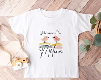May include: White baby onesie with a pink and white bird graphic and the text "Welcome little Melina".