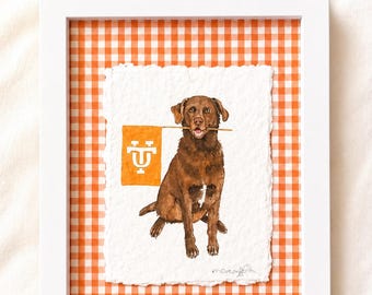 May include: A framed custom pet portrait featuring a brown Labrador Retriever holding a flag with a university logo. The artwork is set against a white and orange gingham background, framed in a white border. Text at the top reads "CUSTOM COLLEGE PET PORTRAIT".