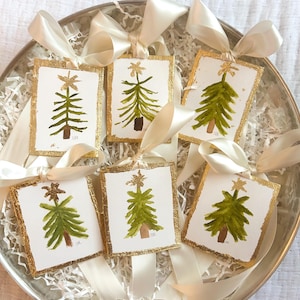 May include: Six handmade Christmas tree ornaments with gold trim and green watercolor paint. Each ornament has a gold star on top and the letters "C&R" at the bottom.