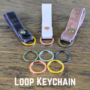 May include: Three leather keychains with metal loops in different colors. The keychains are brown, white, and gray. The loops are gold, silver, and copper.