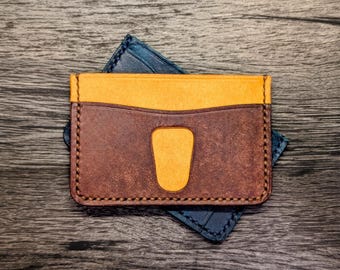 May include: A brown leather wallet with a yellow leather flap and a stitched edge. The wallet is folded in half and has a slot for cards.