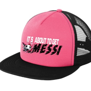 Könnte beinhalten: Rosa-schwarze Trucker-Kappe mit einer weißen Grafik, auf der "It's about to get Messi" mit einem Fußball-Motiv steht.