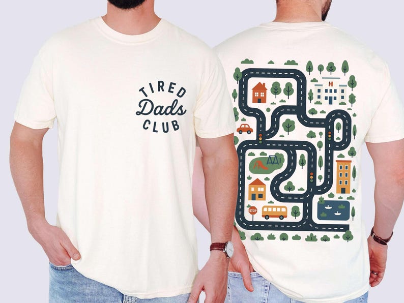 Może przedstawiać: Kremowa koszulka z napisem "Tired Dads Club" z przodu. Tył przedstawia wz&oacute;r mapy drogowej z domami, drzewami, autobusem i samochodem. Projekt jest w odcieniach niebieskiego, pomarańczowego i zielonego.