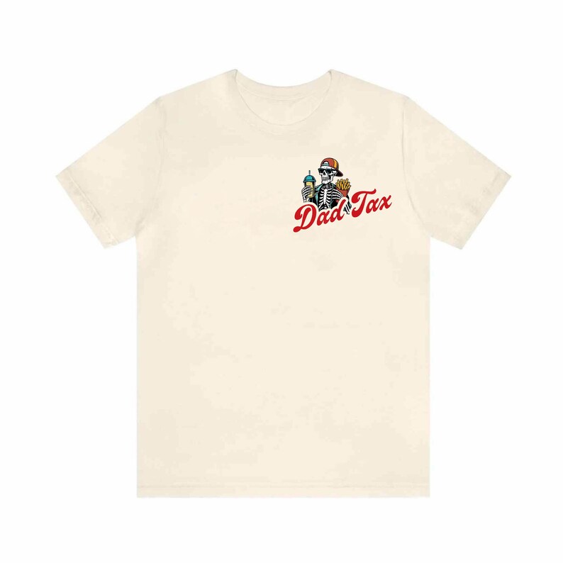 May include: Cream-colored t-shirt featuring a skeleton wearing a red cap and sunglasses, holding a drink and fries. The text "Dad Tax" is printed in red script below the graphic. The shirt is made of a soft material.