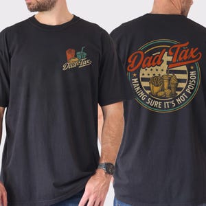 May include: Black t-shirt with front and back graphics. The front graphic says "Dad Tax" with a small illustration of fries, a burger, and a drink. The back graphic says "Dad Tax" in a circle with food illustrations and the text "Making sure it's not poison."