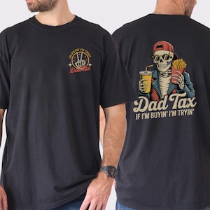 May include: Black t-shirt with a graphic on the front and back. The front graphic says "Dad Tax" with a peace sign. The back graphic features a skeleton with a drink and fries, and the text "Dad Tax" and "If I'm buyin' I'm tryin'".