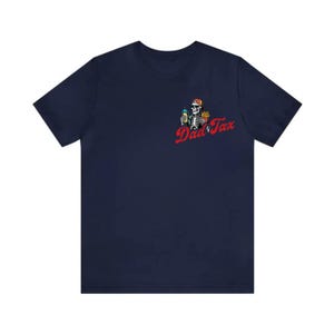 May include: Navy blue t-shirt featuring a skeleton wearing a baseball cap, holding a drink and fries. The text "Dad Tax" is in red script. The graphic is on the left chest area of the shirt.