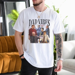 May include: White t-shirt with the text "DAD VIBES" above a graphic of several men. The graphic features a vintage style design. The shirt is a casual, everyday wear item.