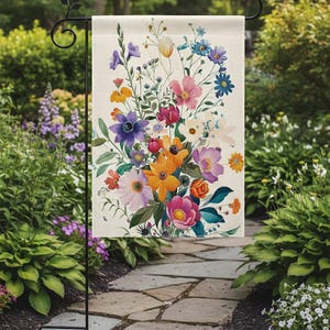 May include: A rectangular garden flag featuring a vibrant floral arrangement in shades of purple, orange, pink, and blue. The flowers are set against a cream-colored background. The flag is displayed on a black metal stand, set in a garden.