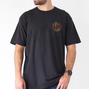 Pu&ograve; includere: T-shirt nero a maniche corte con scollo tondo. La maglietta presenta una piccola grafica sul petto a sinistra con la scritta "Drink Till It Hurts". La grafica &egrave; un teschio con un cappello a cilindro e una bevanda in mano. La maglietta &egrave; indossata da una persona.