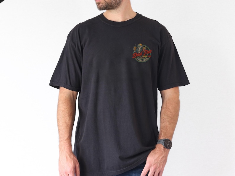 Pu&ograve; includere: T-shirt nero a maniche corte con scollo tondo. La maglietta presenta una piccola grafica sul petto a sinistra con la scritta "Drink Till It Hurts". La grafica &egrave; un teschio con un cappello a cilindro e una bevanda in mano. La maglietta &egrave; indossata da una persona.