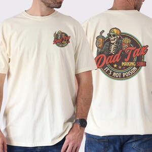 Pu&ograve; includere: T-shirt color crema con grafica sul davanti e sul retro. La grafica anteriore dice "Dad Tax" con uno scheletro. La grafica posteriore presenta uno scheletro con una bevanda e patatine fritte, con il testo "Dad Tax Making Sure It's Not Poison."