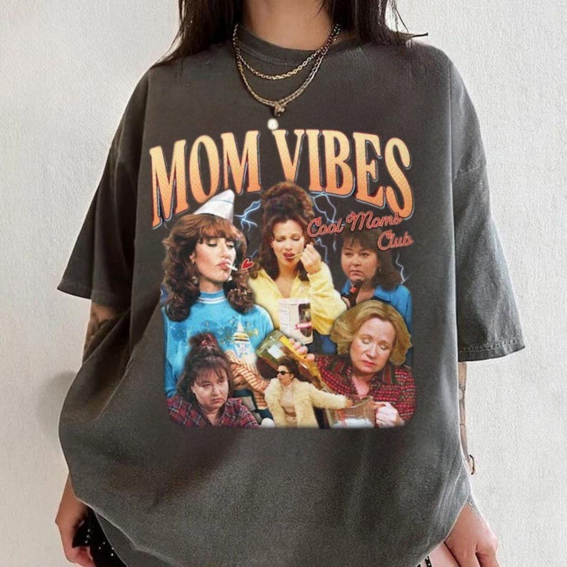 May include: A gray t-shirt with a vintage-style graphic print featuring a group of women with the text "Mom Vibes Cool Moms Club".