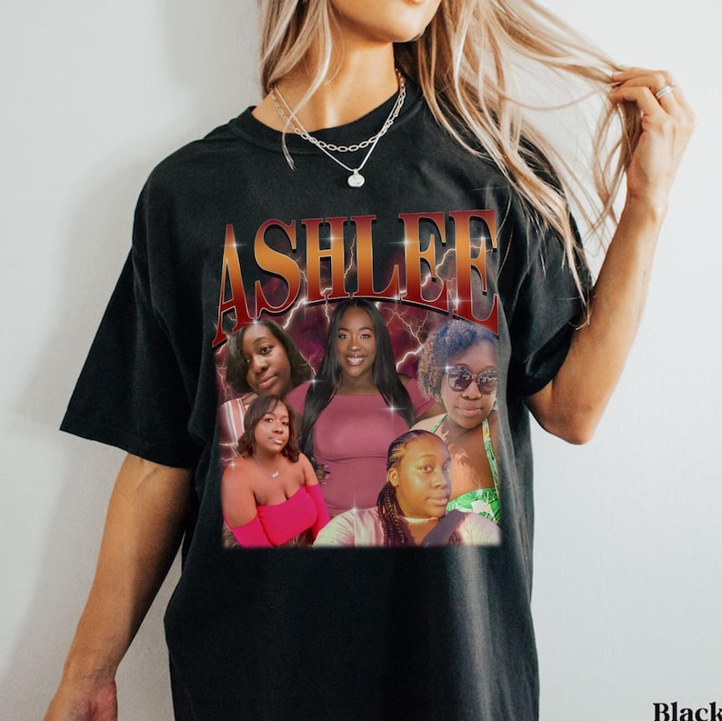 May include: Black t-shirt with a graphic print of the word "ASHLEE" in red and yellow letters with lightning bolts. The graphic also features five women's faces in a collage style.