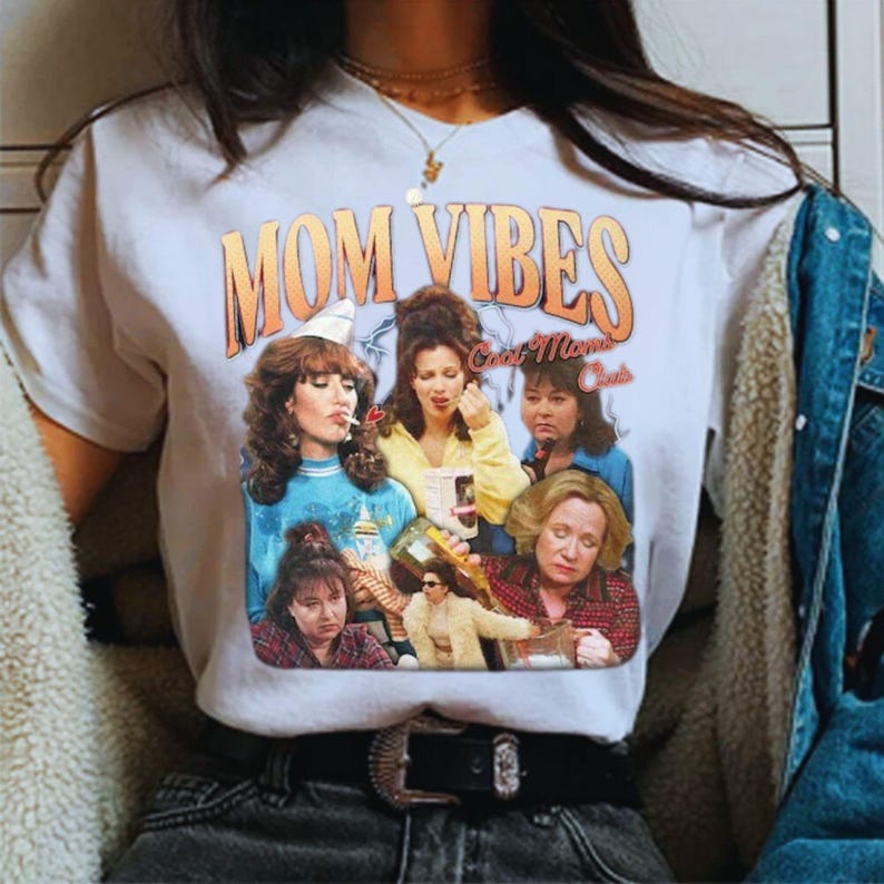 May include: White t-shirt with a graphic print of the "Golden Girls" cast with the text "Mom Vibes" and "Cast Moms Crew".