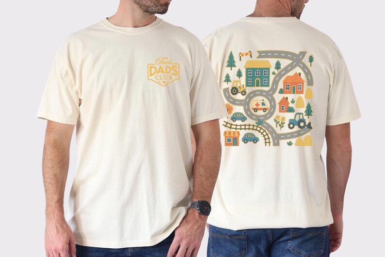 May include: Cream-colored t-shirt with a graphic on the back featuring a road map design with houses, vehicles, and trees. The front of the shirt has a gold-colored "Dads Club" logo. The shirt is made of a soft, comfortable material.