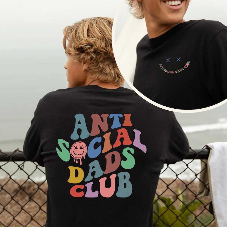 May include: Black long-sleeve shirt with the text "ANTI SOCIAL DADS CLUB" in colorful, retro-style lettering on the back. The front of the shirt has a small smiley face and the words "ANTI SOCIAL DADS CLUB".